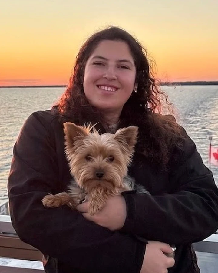 Rasha holding a small Yorkshire terrier on a ferry at sunset